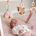 Baby ligt onder houten babygym met speeltjes: bloem, hertje en aardbei.