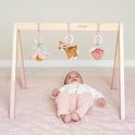 Baby ligt onder houten babygym met speeltjes: bloem, hertje en aardbei.
