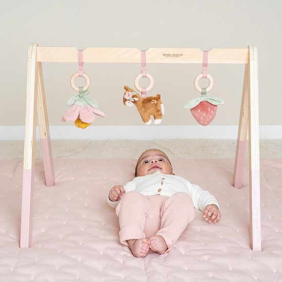 Baby ligt onder houten babygym met speeltjes: bloem, hertje en aardbei.