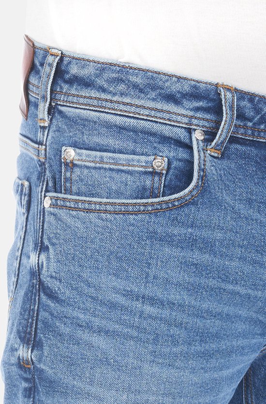 Close-up van de voorkant van een blauwe spijkerbroek met een bruin LTB leren label en een kleine zak met metalen studs.