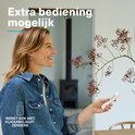Vrouw met blonde haren, blauwe spijkerjas, houdt witte afstandsbediening vast. "Extra bediening mogelijk."