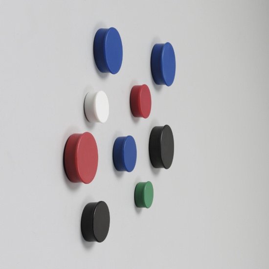 Een reeks ronde magneten in verschillende kleuren: blauw, wit, rood, zwart en groen, bevestigd aan een grijze muur.