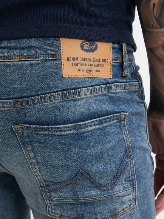 Achterkant van een blauwe spijkerbroek met Petrol Industries 'Denim Driven Since 1989' label op de heup.