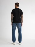 Man met tatoeages, achterkant van zwarte t-shirt en blauwe jeans.