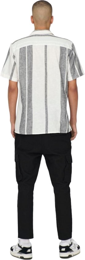 Man in wit hemd met verticale grijs-witte strepen, zwarte cargo broek.