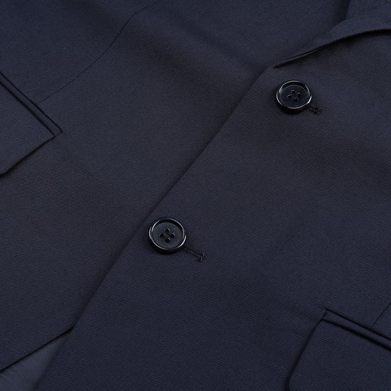 Sluiting met twee knopen van de donkerblauwe blazer, met steekzakken.