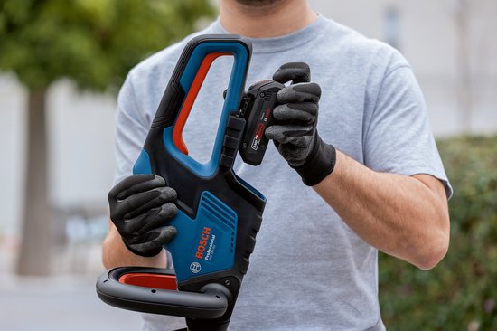 Man in grijze trui en zwarte handschoenen plaatst een Bosch accu in een blauw-zwarte heggenschaar.