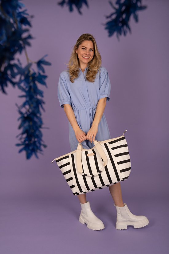 Blonde vrouw in blauwe jurk met gestreepte tas, met blauwe bloemen op de voorgrond.