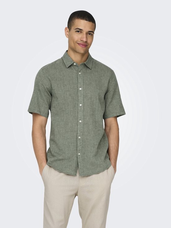 Een man in een lichtgroen linnenmix overhemd met korte mouwen en beige broek, lachend.