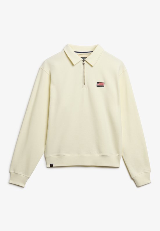 Off-white trui met halve rits, kraag en een rode, witte en blauwe patch op de borst.