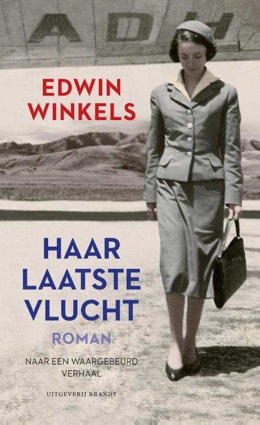 Vrouw in grijs mantelpak en bijpassende hoed, met tas in de hand, voor landschap met "AD"