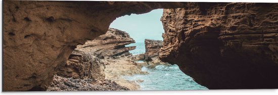 WallClassics - Dibond - Uitzicht op Strand en Zee van onder de Rotsen - 90x30 cm Foto op Aluminium (Met Ophangsysteem)