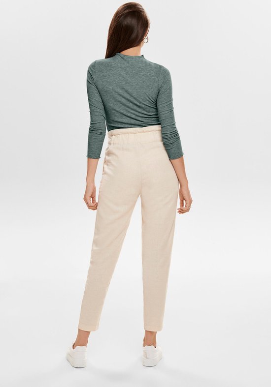 Model draagt een grijze coltrui met lange mouwen, geribde textuur, gegolfde kraag en een lichte broek met hoge taille.