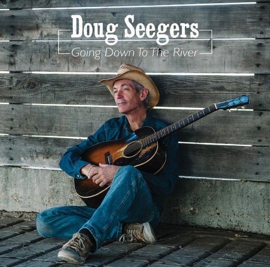 Doug Seegers, zittend met gitaar, draagt een cowboyhoed, spijkerblouse en spijkerbroek.