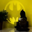 Zwart silhouet van de Batman figurine op de spotlight, die het Bat-signaal op de gele muur projecteert.
