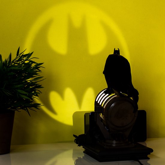 Zwart silhouet van de Batman figurine op de spotlight, die het Bat-signaal op de gele muur projecteert.