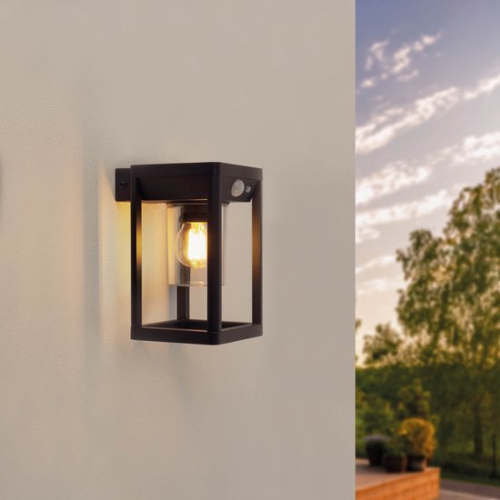 Zwarte vierkante wandlamp met een glazen cilinder en een zichtbare lichtbron, bevestigd aan een witte muur.
