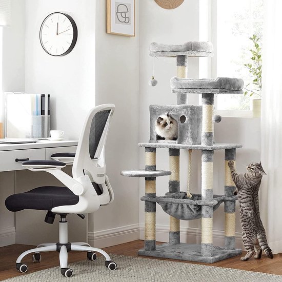 Grijze kattenkrabpaal met huisje en plateaus, naast een bureau. Een cyperse kat krabt aan de paal.
