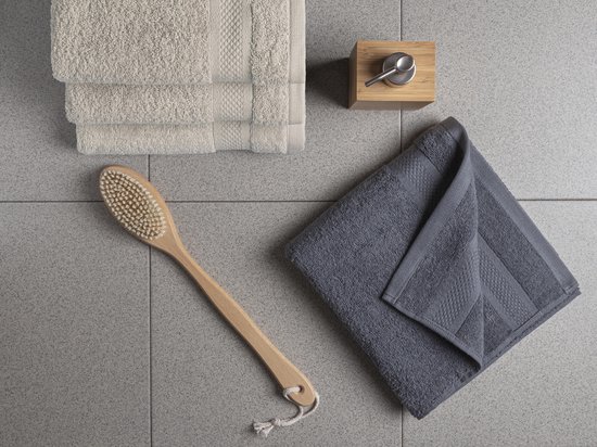 Overzicht van badkamerartikelen: opgevouwen beige handdoeken, een grijze handdoek, houten borstel en zeepdispenser.