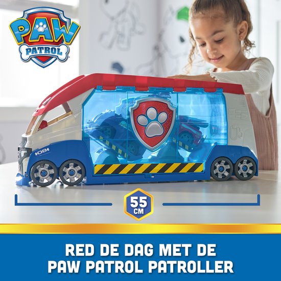 Een meisje opent het Luik van de PAW Patrol Patroller, een groot blauw, wit en rood voertuig met transparante deuren.