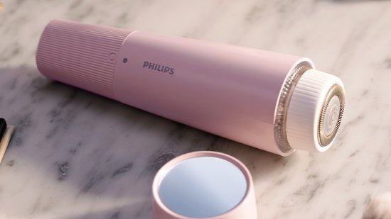 Roze Philips gezichtshaarverwijderaar met een LED-ring en scheerkop, naast een ronde roze spiegel op een marmeren ondergrond.