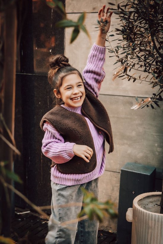 Lachend meisje draagt een bruin teddy fleece gilet en paarse trui, met opgestoken haar.
