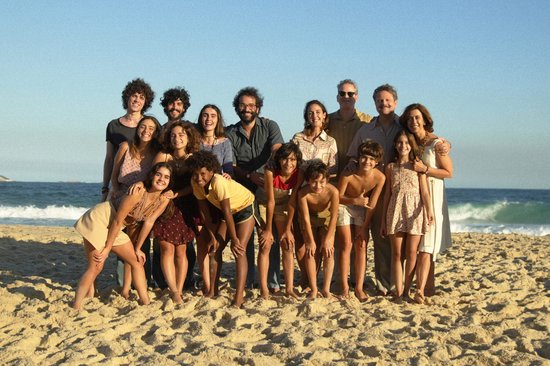 Groepsfoto van 15 personen op het strand, met de oceaan op de achtergrond.