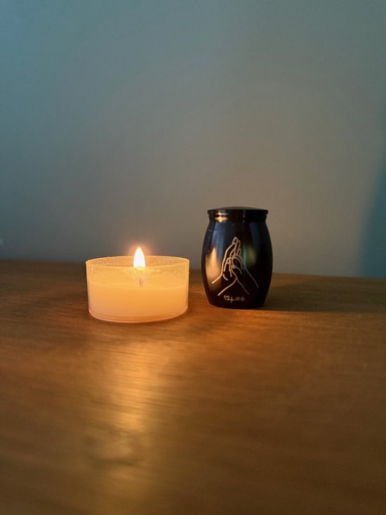 Zwarte mini urn met pootafdruk opdruk, naast een brandend kaarsje.