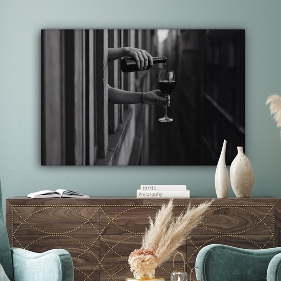 Zwart-wit canvas van handen die wijn schenken boven een houten dressoir met vazen en boeken.