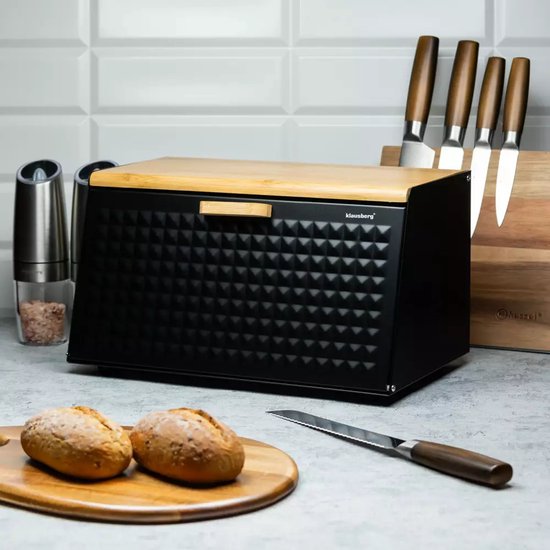 Boîte à pain noire Klausberg avec couvercle en bambou, posée sur un comptoir à côté de petits pains et d'ustensiles de cuisine.