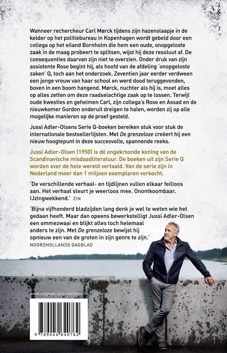 Een man in een zwart leren jack, jeans en wit T-shirt staat met de armen over elkaar. Achter hem een waterig landschap.