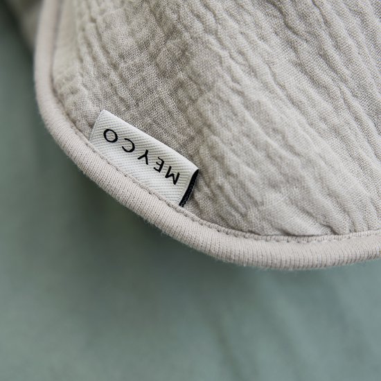 Label 'Meyco' op de lichtgrijze stof van een babyslaapzak.