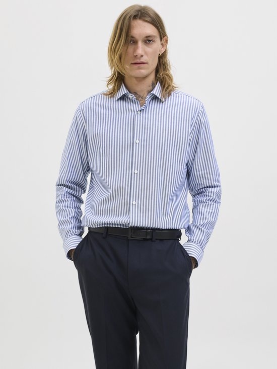 Man met handen in de zakken, draagt een blauw-wit gestreept overhemd en een zwarte riem.