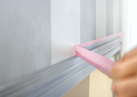 Roze schilderstape wordt aangebracht op een grijze en witte gestreepte muur, met een grijze sierlijst.