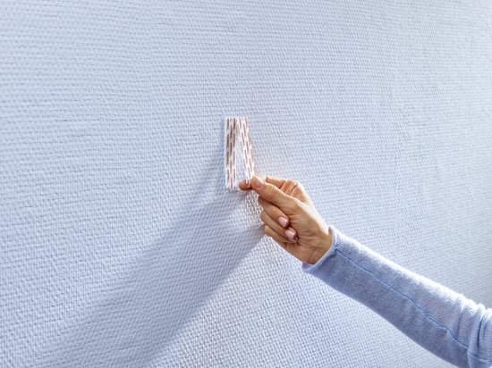 Main retirant un tesa Powerstrip d'un papier peint texturé.