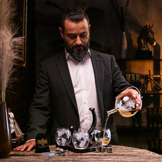 Man schenkt whisky uit wereldbol karaf in wereldbol glas. Set met glazen en stenen.