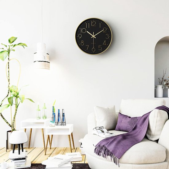 Zwarte wandklok met gouden rand en cijfers, hangend aan een muur in een modern ingerichte woonkamer.