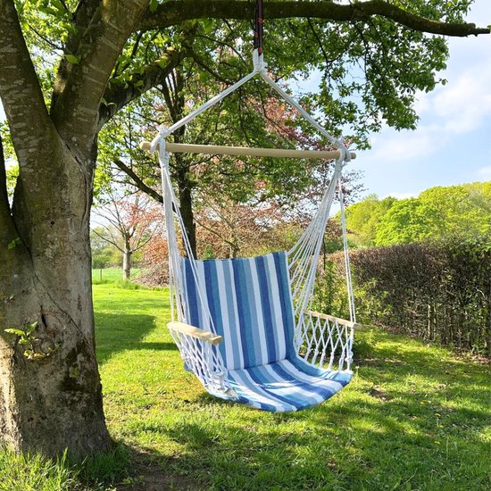 Blauw-witte gestreepte hangstoel met houten armleuningen, hangend aan een boom in een groene tuin.