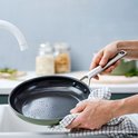 Handen wassen een olijfgroene hapjespan onder de kraan.