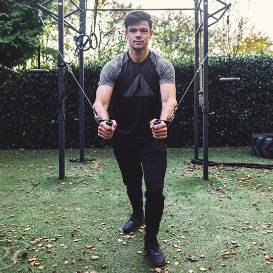 Man doet borstoefeningen met het Ruffman fitness kabelsysteem in een buitenomgeving.