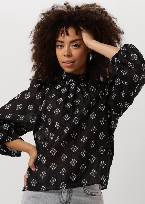 Model draagt een zwarte blouse met opstaande kraag en wit bloemenpatroon.