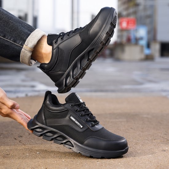 Zwarte werksneakers, een aan de voet, de ander in de hand.