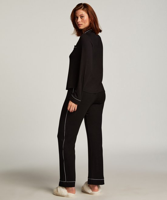 Model met rood haar draagt een zwarte pyjamaset met witte biezen en fluffy slippers.