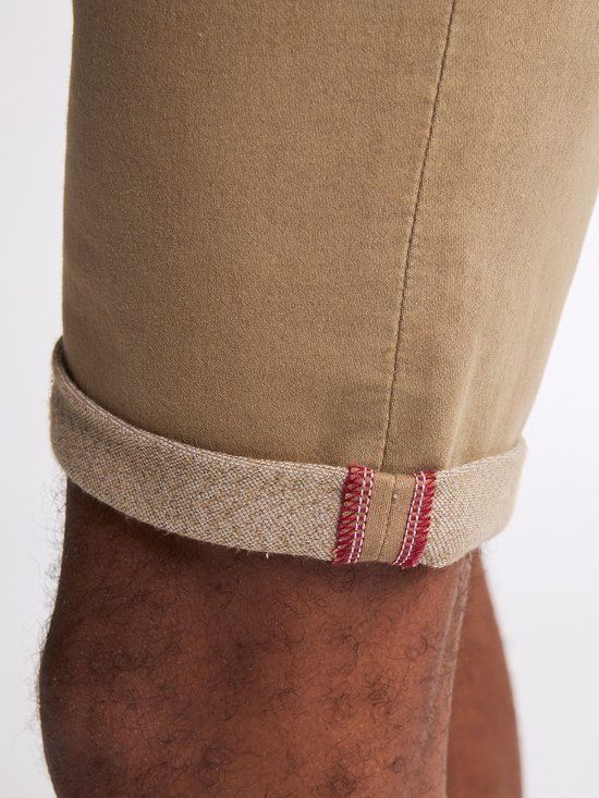 Close-up van de omgeslagen zoom van een bruine chino met een rode, geborduurde bies.