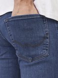 Close-up van de achterzak van een blauwe slim fit jeans met bruine stiksels.