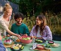 Een vrouw schept salade uit een roze kom tijdens een buitenmaaltijd met vrienden.