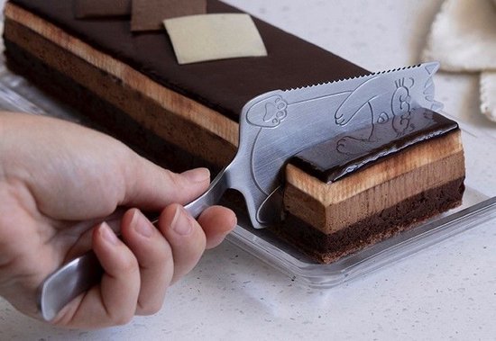 Zilverkleurige taartschep met kattenpootjes, die een stuk chocoladetaart serveert.