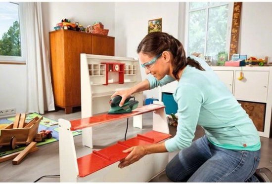 Vrouw met veiligheidsbril schuurt een witte en rode plank met een groene Bosch multischuurmachine.