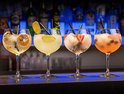 Vier gevulde cocktailglazen met fruitgarnituren en rietjes op een bar.