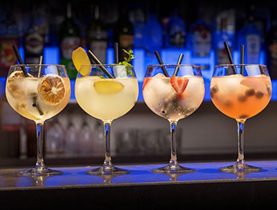Vier gevulde cocktailglazen met fruitgarnituren en rietjes op een bar.
